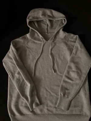 Grå Kashmir Hoodie xs/s - En stilren grå kashmir hoodie med huva och snörning. Tröjan har långa ärmar och ribbade muddar vid ärmslut och nederkant. Perfekt för chill dagar och enkel att matcha med jeans eller joggers.