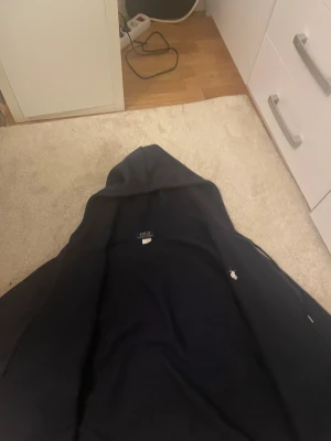 Mörkblå hoodie från Polo Ralph Lauren - Snygg mörkblå hoodie från Polo Ralph Lauren med klassisk logga broderad på bröstet. Tröjan har huva med snörning, dragkedja och två fickor framtill. Perfekt för chill dagar och enkel att matcha med jeans eller joggers. I storlek L fast passar perfekt för dig om du är 175 ungefär