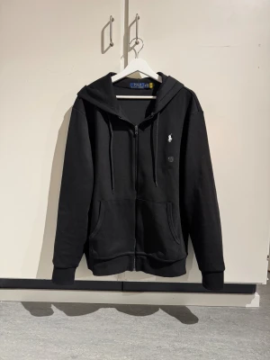 Svart zip hoodie Ralph Lauren - Svart zip hoodie från Ralph Lauren. Tillverkad i mjuk bomull, perfekt för chill dagar. Klassisk och stilren look. Tveka inte att skriva vid frågor!
