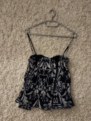 Svartvit blommig linnetopp H&M XS - Säljer en svartvit linnetopp från H&M i storlek XS. Toppen har tunna axelband, plisserad struktur och ett blommigt mönster. Materialet är lätt och luftigt, perfekt för varma dagar. Snyggt flowy fall och passar dig som gillar stilrena kontraster.