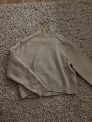 Beige polotröja från H&M i stickad bomull - Säljer en beige polotröja från H&M i stickad bomull. Tröjan har en hög ribbad krage, långärmade ärmar och ribbade muddar vid ärmslut och nederkant. Perfekt för lager-på-lager och chill stil under höst och vinter.