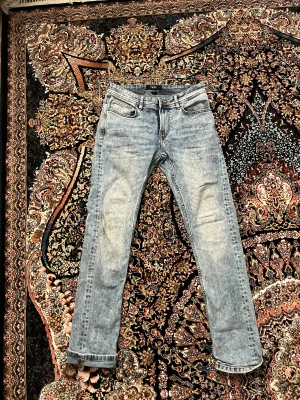 Ljusblå jeans från Smog Original - Säljer ett par ljusblå jeans från Smog Original med snygg tvättad look. Klassisk femficksmodell, raka ben och normal passform. Jeansen har detaljerade sömmar och läderpatch bak i midjan. Perfekt för dig som gillar stilrena och avslappnade jeans. Köpte den från new Yorker för 230kr