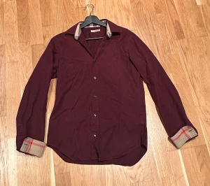 Vinröd skjorta från Burberry - 📏 Storlek: S Är 175 och tycker den passar perfekt  ✨ Passform: Slim 🎨 Färg Vinröd 🧵 Material: Bomull  💎 Skick: Fint skick alla knappar är intakta och sitter bra den har lite solblekning om man tittar noga på kragen men annars inga problem.  🔍 Detaljer: 	Perfekt skjorta allmänt har haft den ofta på mig och tagit hand om den varsamt varje gång jag har haft den på mig ha tjat fått komplimanger så det är en skjorta som fångar mycket blickar.
