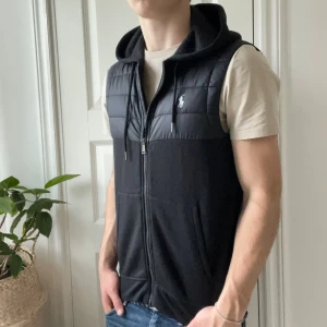 Ralph Lauren väst  - Ralph Lauren väst svart med luva och spännen. Hur najs som helst! Modellen är 180 cm 75 kg och bär storlek S. Kom med frågor 🌟