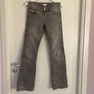 Grå bootcut jeans med broderade fickor - Säljer ett par gråa jeans med bootcut passform och snygga broderade detaljer på bakfickorna. Klassisk femficksmodell med knapp och dragkedja framtill. Jeansen har en lite utsvängd siluett och är tillverkade i mjukt jeanstyg. Lite slitna vid benen.