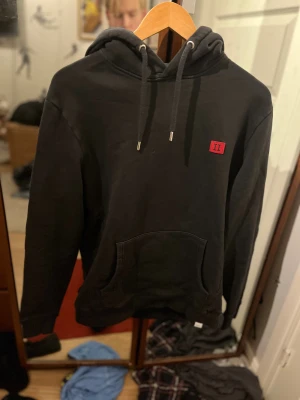 Svart hoodie med röd II-patch - Svart les deux hoodie med huva. Klassisk känguruficka framtill och ribbade muddar. stilren design som passar perfekt till vintern.