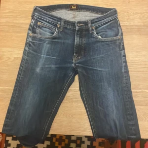 Mörkblå jeans från Lee, straight fit - Säljer ett par mörkblå jeans från Lee, de har hål vid innerbenet men väldigt litet.  Slitningar som kommer från 3 års användning. Jeansen har raka ben och kontrastsömmar i gult. Modellen kallas daren zip fly.