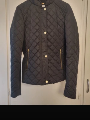 Svart jacka från Vila XS - Sart jacka från Vila i storlek XS. Jackan har guldfärgade dragkedjor på fickorna och knappar framtill. Snyggt rutmönster och är perfekt för vår/höst 🥰