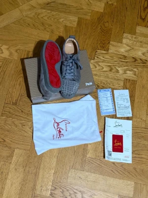 Grå Christian Louboutin sneakers med nitar - Säljer ett par grå sneakers från Christian Louboutin med coola nitar på tån och klassisk röd sula. Skorna är i mocka och har snörning samt rund tå. Kommer med originalkartong, dustbag och äkthetsbevis. Perfekt för dig som vill sticka ut med lyxig streetstyle.