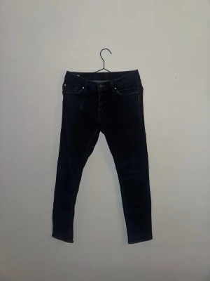 Mörkblå skinny jeans från T/J - Snygga mörkblå skinny jeans med klassisk femficksdesign och smal passform. Jeansen har midwaist och är tillverkade i stretchigt denimmaterial för extra komfort. Perfekta att matcha med sneakers eller boots för en cool look.