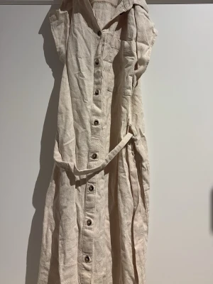 Beige långklänning med knappar - Säljer en lång beige klänning med knappar. Ett snöre vid midjan så att man kan knyta en söt rosett i mitten eller bara en vanlig knut. 