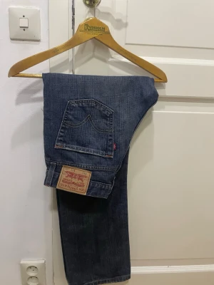 Levi's 514 mörkblå jeans - Säljer ett par klassiska Levi's 514  jeans i mörkblå tvätt. De har raka ben, fem fickor och den ikoniska läderpatchen bak. Jeansen är tillverkade i slitstarkt bomullsmaterial och har en normal passform. Perfekta för dig som gillar tidlös stil och vill ha ett par schyssta jeans. 