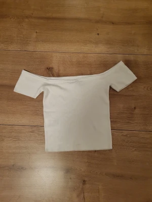 Vit offshoulder topp - Säljer en stilren vit offshoulder topp med korta ärmar. Toppen har en rak och tight passform som sitter snyggt över axlarna. Perfekt att matcha med jeans eller kjol för en enkel och fräsch look.