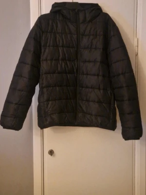Svart pufferjacka från H&M, storlek L - Svart pufferjacka från H&M i storlek L. Jackan har huva, horisontella quiltade sömmar och dragkedja framtill. Materialet är syntet och jackan är långärmad med en loose passform. Perfekt för kyliga dagar och enkel att matcha med olika outfits. Lite nopprig längst ner samt ett litet, litet hål på höger arm. I övrigt mkt fint skick. 