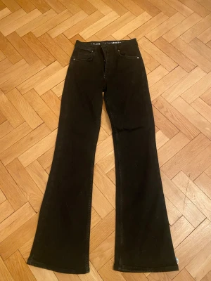 Boot flare jeans från Never Denim - Svarta boot flare jeans från Never Denim med klassisk femficksdesign och utsvängda ben. Jeansen har normal passform och är tillverkade i jeansmaterial. Snyggt läderpatch med logga bak i midjan. Perfekta för dig som gillar retrovibbar och vill ha en cool siluett.