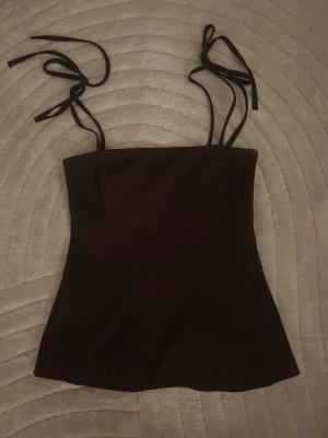Brun linnetopp med knytband - Säljer en brun linnetopp med smala axelband som knyts på axlarna. Toppen har en enkel och stilren design med lätt utsvängd nederkant. Perfekt att styla med jeans eller kjol för en cool look.