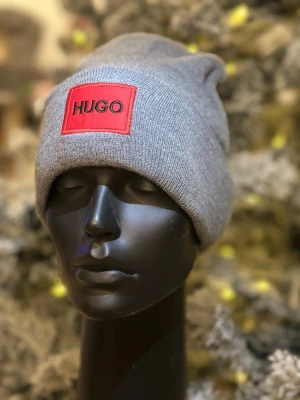 Grå väst från Hugo med röd logga - Snygg grå väst från Hugo med en tydlig röd logga framtill. Västen har en enkel och stilren design som passar perfekt till lager-på-lager-stil. Tillverkad i mjukt stickat material som känns skönt mot huden.