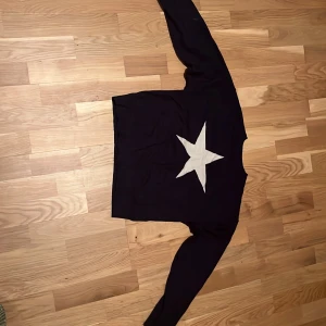 Svart tröja med stjärna från Gina Tricot - Säljer en svart långärmad tröja från Gina Tricot med en stor vit stjärna på framsidan. Tröjan har en klassisk passform och är gjord i mjukt material, perfekt för dig som vill ha en enkel men ändå statement look. Har använt fåtal gånger.