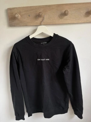 Svart sweatshirt från ON THAT ASS - Svart sweatshirt från ON THAT ASS i storlek M. Tröjan har rund hals, långärmade ärmar och vit text på bröstet. Materialet är mjuk bomull och passformen är normal. Perfekt för chill dagar och enkel att matcha med jeans eller joggers.