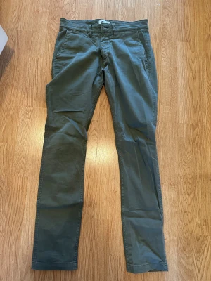 NN07 Gröna chinos - Märke:NN07 Snygga gröna chinos med klassisk rak passform och diskreta fickor både fram och bak. Byxorna har en enkel design och är gjorda i mjukt bomullsmaterial som är skönt att bära. Perfekta för dig som gillar stilrena och bekväma byxor.