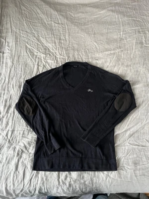 Svart grå v-ringad tröja från LJUNG - Svart/grå v-ringad merinoull tröja från LJUNG i storlek M. Tröjan har lång ärm och snygga förstärkningar på armbågarna i svart mocka liknande material. Enkel och stilren design med liten broderad logga på bröstet. Perfekt till lager på lager under höst och vinter. Stor i storleken. || Fråga på om det är något!