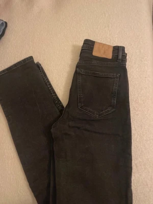 Svarta jeans från Zara - Säljer ett par svarta skinny jeans från Zara med klassisk femficksdesign och hög midja. Jeansen har silverfärgad knapp och nitar, samt en diskret tvättad look. Materialet är stretchigt jeans och passformen är tight hela vägen ner.