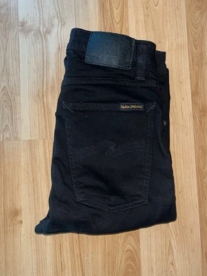 Nudie Jeans - Snygga svarta skinny jeans från Nudie Jeans. Materialet är mjukt och stretchigt bomullstyg som sitter tajt och bekvämt. Midja 29cm, längd 95cm. JAG SKICKAR EJ FLER BILDER NÄR JAG BÄR JEANSEN! för bättre inblick i passformen rekommenderar jag att googla på modellnamnet. För storleksguide kolla måtten noggrant då jeansen alltid kan vara uppsydda heller krympta och jag ej tar emot returer :) s5,4