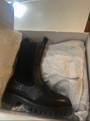 Svarta chunky chelsea boots - Säljer ett par snygga svarta  boots med chunky sula från nakd. Bootsens ovandel är i skinn och är helt nya. Perfekt för dig som gillar en stilren och edgy look. Skorna är köpta för ca 800 kr. Storlek 36-37
