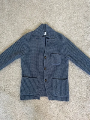 Blå stickad kofta från Gran Sasso - Säljer en chunky blå stickad kofta från Gran Sasso med grov ribbstickning, tre framfickor och stora knappar. Koftan har en bred krage och långärmade ärmar, perfekt för kyliga dagar. Italiensk design med klassisk look. Nypris 3600kr och denna färg är slutsåld så sällsynt kofta!