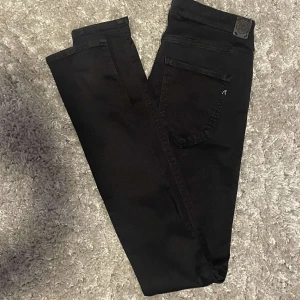 Svarta slimfit Replay Hyperflex jeans - Säljer ett par svarta Replay Hyperflex jeans med klassisk femficksdesign och snygga detaljer som Replay-logga på fickan och bak. Jeansen är stretchiga och har en slim fit passform som sitter riktigt snyggt. Perfekta för dig som gillar stilrena och bekväma jeans.