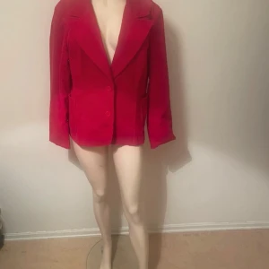 Röd manchesterkavaj med knappar - Snygg röd kavaj i manchester med klassisk krage och två stora knappar framtill. Jackan har raka, långa ärmar och två fickor på sidorna. Perfekt för dig som vill sticka ut med färg och struktur.