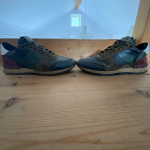 Valentino Garavani Rockrunner sneakers - Snygga Valentino Garavani Rockrunner sneakers i camouflagemönster med inslag av grönt, brunt, svart och vinrött. Skorna har detaljer i mocka och skinn, klassisk snörning och ikoniska nitar på hälen. Perfekta för dig som vill sticka ut med lyxig streetstyle.