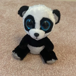 Ty Beanie Boo Bamboo Panda - Söt Ty Beanie Boo Bamboo panda med stora blå glittriga ögon. Mjuk plysch, svart och vit, i mycket fint skick utan synligt slitage. Perfekt för samlare eller som present till barn. Originaletikett kvar på sidan.