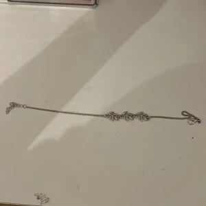 Silverfärgat armband med bladmotiv - Ett stilrent armband till benet i silverfärg med detaljerade bladmotiv i mitten. Kedjan är tunn och smidig med ett klassiskt spänne. Perfekt för dig som gillar naturinspirerade accessoarer och vill ha något som sticker ut lite extra. Aldrig använt 