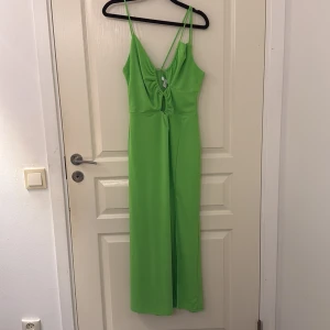 Limegrön långklänning med smala axelband - Snygg limegrön långklänning med smala axelband och v-ringning. Klänningen har en rynkad detalj framtill och en liten cut-out under bysten. Materialet är slätt och stretchigt, perfekt för sommarens varma dagar.