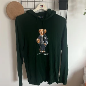 Mörkgrön hoodie från Polo Ralph Lauren - Mörkgrön hoodie från Polo Ralph Lauren med ikoniska Polo Bear-trycket på bröstet. Långärmad modell med huva och snörning. Tillverkad i mjuk bomull. Skickar innom 24-48h om tid finns. Du kan kontakta mig för prisförslag! Finns ett mini hål vid lappen men syns knappt💕
