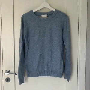 Blå stickad tröja från Vila - Mysig blå stickad tröja från Vila med rund halsringning och ribbade muddar vid ärmslut och nederkant. Knappt använd.