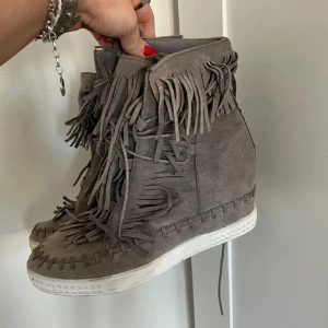 Grå mockasneakers med fransar - Säljer ett par isabel marant liknande khakigröna skor i mocka med coola fransdetaljer runt skaftet och längs snörningen. Skorna har vit sula och dekorativa sömmar längs kanten. Sååå söta! Pris går att diskutera!