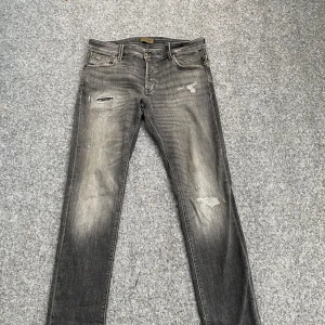 Svarta slim jeans - Svarta jeans med slitningar och snyggt tvättad look. Modellen är slim fit med smal passform och klassiska fem fickor. Jeansen har dragkedjegylf och detaljerade bakfickor. Perfekta för dig som gillar en lite ruffare stil. Hör av dig vid fler funderingar!