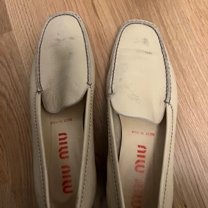 Beige vintage loafers från Miu Miu i skinn - Snygga beige vintage loafers från Miu Miu med fyrkantig tå och diskreta sömmar. Skorna är tillverkade i mjukt skinn och har en platt sula. Perfekta för dig som gillar minimalistisk och stilren design med italiensk känsla.