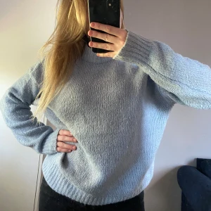 Ljusblå stickad tröja med rund hals - Mysig ljusblå stickad tröja med rund halsringning och långa ärmar. Tröjan har en relaxed passform och breda ribbade muddar vid ärmslut och nederkant. 