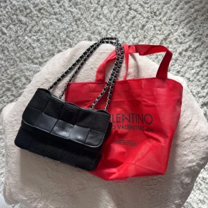 Svart väska från Valentino - Snygg svart axelväska från Valentino med flätad design i skinn och tyg. Väskan har en kedjerem i silver och svart. Kan ha den både över axeln och crossbody. Fortfarande super fin och i jätte bra skick, bara själva valentino texten som är lite bortskavd(se sista bilen) pris kan diskuteras vid snabb affär.
