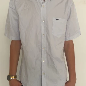 Vit kortärmad skjorta Hampton Republic - Vit kortärmad skjorta från Hampton Republic med klassisk krage, bröstficka med broderad logga och knäppning framtill. Regular fit och tillverkad i bomull, perfekt för en clean och stilren look. Sträcker den innan den skickas💕