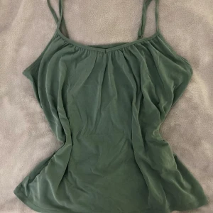 Grön linnetopp från Vero Moda - Snygg grön linnetopp från Vero Moda med tunna axelband och lätt rynkad detalj vid halsringningen. Toppen har en enkel och stilren design som är perfekt för varma dagar. Mjuk och skön känsla mot huden.