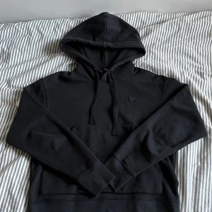 Acne hoodie - Svart hoodie från Acne Studios, Tröjan har huva med snörning, en stor magficka och diskret logopatch på bröstet. Tillverkad i 100% bomull för en skön och avslappnad känsla. Perfekt för dig som gillar stilrena och minimalistiska plagg.