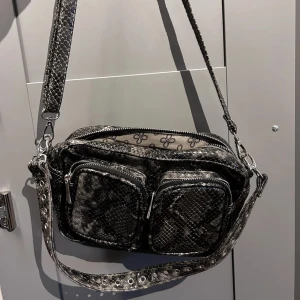 Nuuno inspirerad väska - Väska i ormskinn med flera olika fack. Ett justerbart band och ett kortare axelband. Säljes pga flytt och är i mycket bra skick 