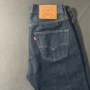 Levi's 501 mörkblå jeans W30 L30 - Klassiska Levi's 501 jeans i mörkblå denim med raka ben och femficksmodell. Snygga kontrastsömmar, knappgylf och ikonisk läderpatch bak i midjan. Perfekta för dig som gillar tidlös stil och vill ha ett par jeans som funkar till allt.  Använt kanske 1-2 gånger och den har legat i min garderob sedan dess. Finns digital kvitto från Boozt om ni begär det. Säljer eftersom den passade inte mig. 