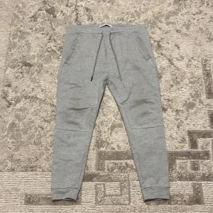 Grå mjukisbyxor från Zara med snörning - Grå mjukisbyxor från Zara i storlek L. Byxorna har snörning i midjan, två fickor fram och två bakfickor. Tillverkade i mjukt bomullsmaterial och har en slim passform med muddar vid bensluten. Perfekta för en chill och avslappnad stil.