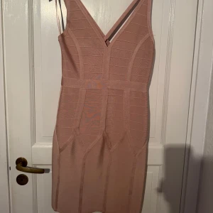 Beige omlottklänning från Topshop - Säljer en snygg beige kortklänning från Topshop med omlott-design och smala axelband. Klänningen har en v-ringad front och markerad midja, tillverkad i ett stretchigt syntetmaterial med struktur. Dragkedja baktill för enkel påklädning. Perfekt för dig som gillar stilrena detaljer.