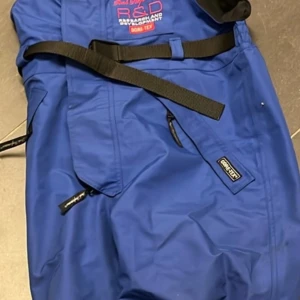 Blå täckbyxor Peak Performance M - Vintage 80-tal, blå skid/täckbyxor från Peak Performance med svarta hängslen och bälte i midjan. Byxorna är tillverkade i slitstarkt Gore-Tex-material och har flera dragkedjeförsedda fickor. Perfekta för vinterns alla äventyr och outdooraktiviteter.